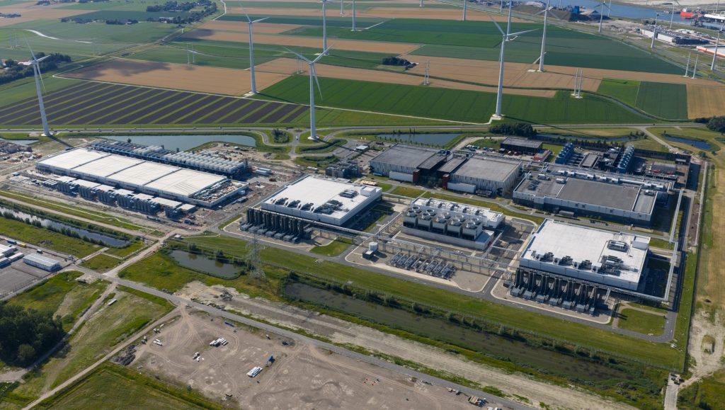 Data center next to agricultural fields, with wind turbines and a coastal town in the background.