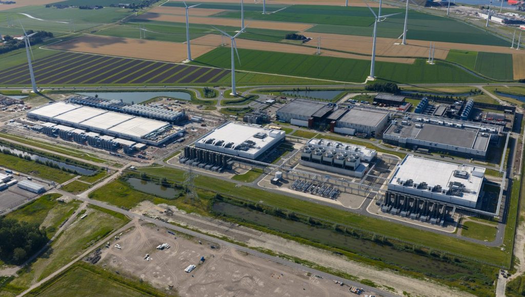 Data center next to agricultural fields, with wind turbines and a coastal town in the background.